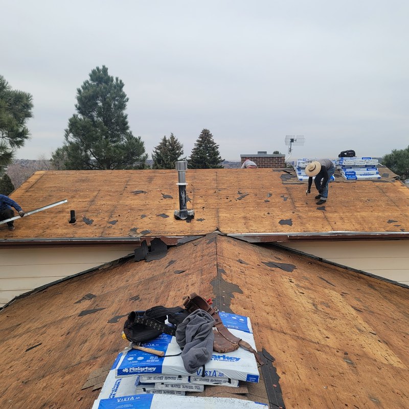 Roofers stripping old shingles from a ridge during a tear-off