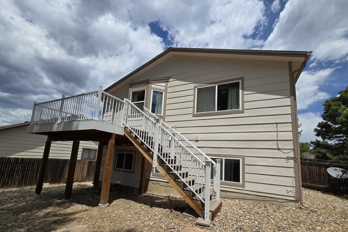 Tan house with a deck staircase and gutters running to grade