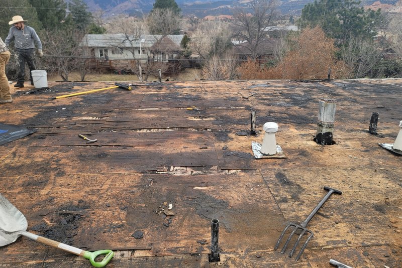 Roof stripped back to bare deck partway through a tear-off, old material cleared aside