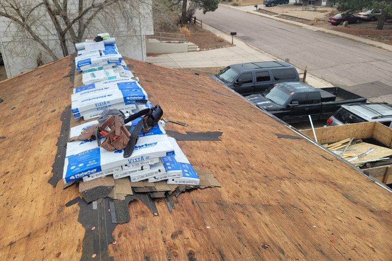 Roofing underlayment and tools staged on bare roof sheathing above a driveway