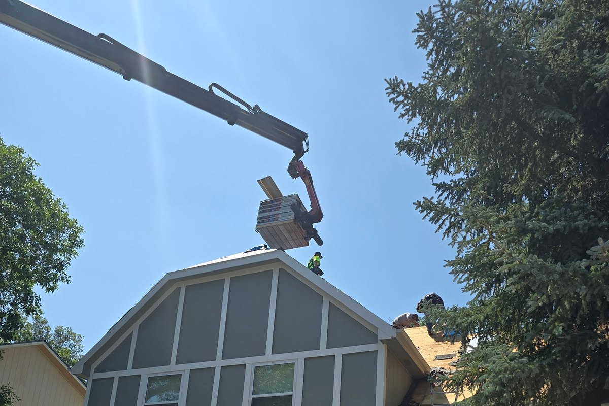 Crane lifting siding to the gable of a gambrel-roof house during installation