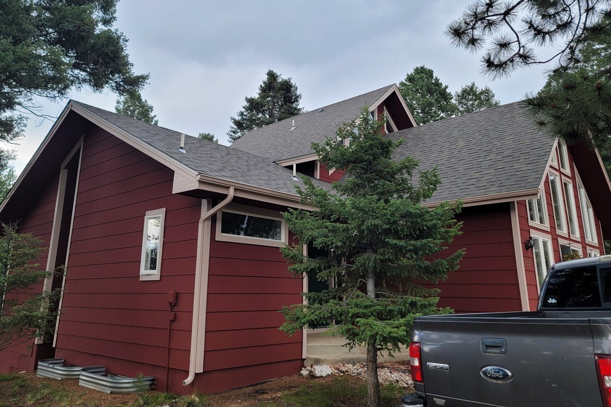 Dark red house with contrasting trim surrounded by tall Colorado pines