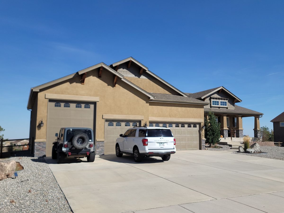 Tan stucco home with a three-car garage, finished shingle roof, and a broad concrete driveway