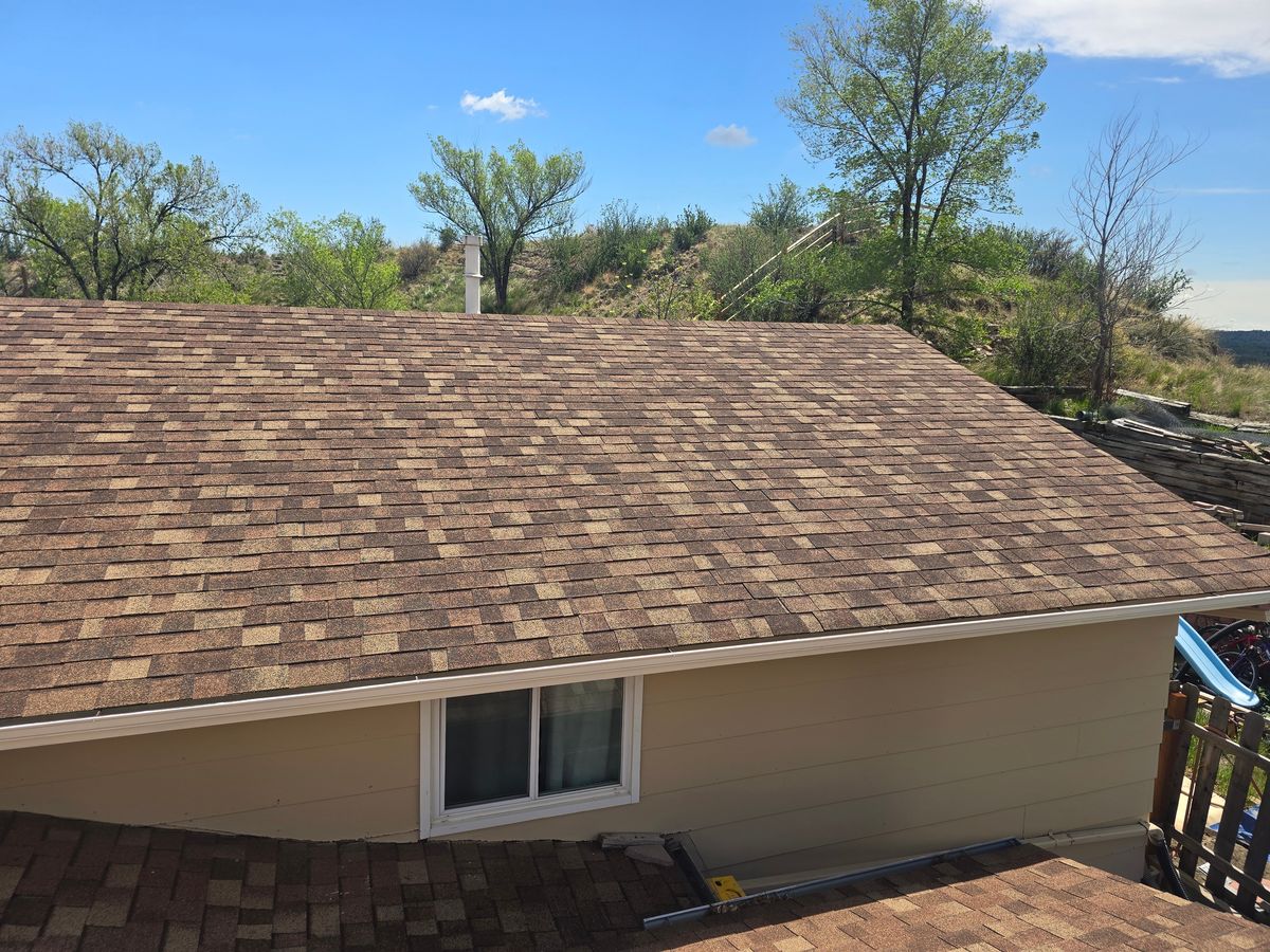 Brown shingle roof above a tan wall with a window