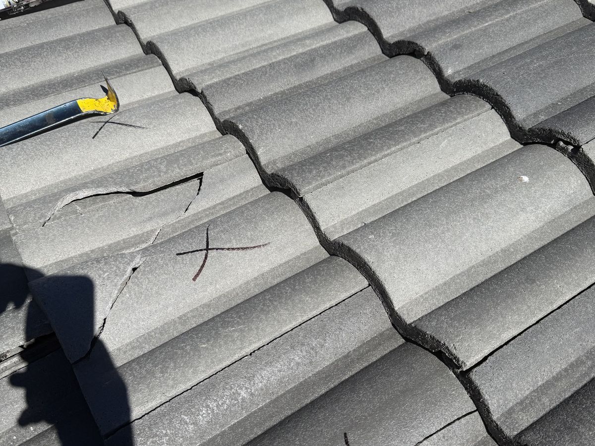Close view of cracked roof tiles with dark marks and a pry bar