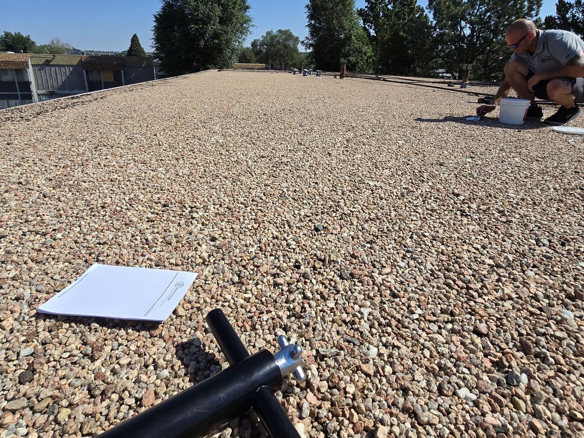 Gravel-covered roof with roof penetrations, a worker, and tools