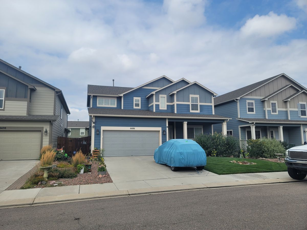 Blue-gray house front with a covered vehicle in the driveway