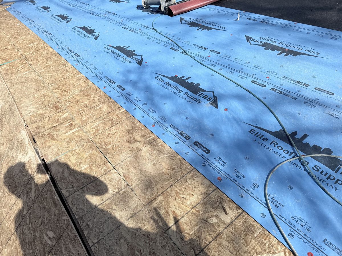 Blue synthetic underlayment rolled out across a stripped roof deck