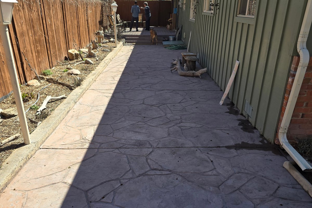 Decorative concrete walkway with a flagstone pattern beside a fence