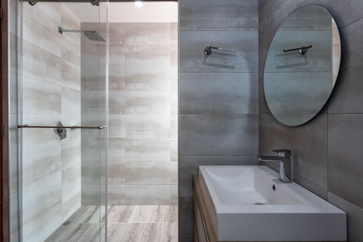 Finished modern bathroom with a glass shower, tiled walls, vanity, and round mirror