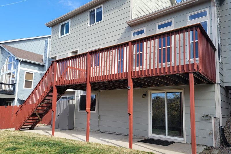 Raised deck with stained boards and railings on a tan two-story house