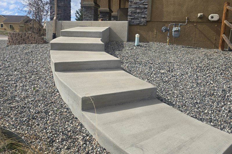 Poured concrete steps and a walkway curving toward a house entrance
