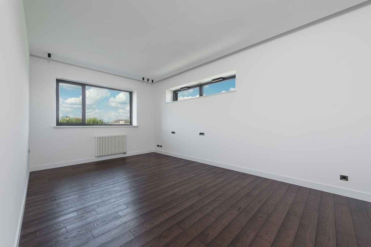 Empty finished room with clean white walls, dark wood flooring, and large windows