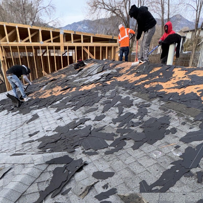 Crew stripping shingles from a roof with the Front Range behind them